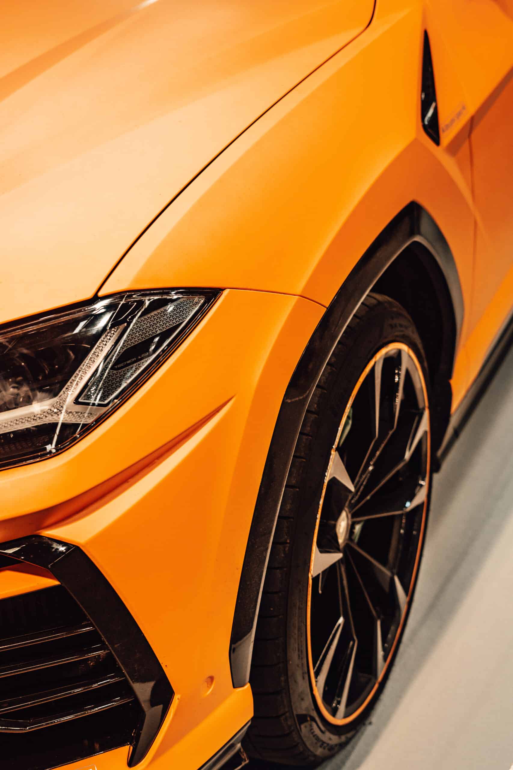 Detail of the front wheel of an orange sports car where you can see part of the front light, against white background